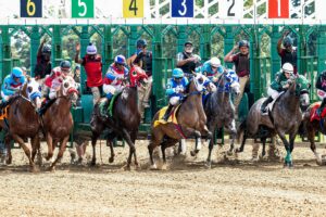 Dynamic scene of jockeys and horses launching from starting gate in a competitive race.